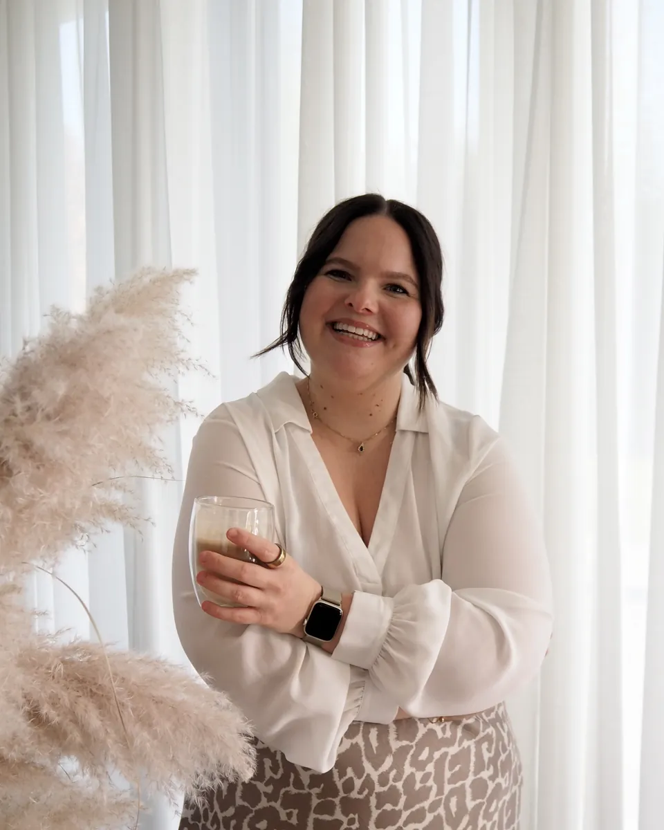 Vivien Jozefowitz lacht in die Kamera, mit einer Tasse Kaffee in der Hand, vor hellen Vorhängen und Pampasgras